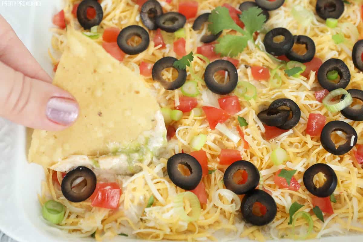 Seven layer bean dip with a tortilla chip being dipped into it.