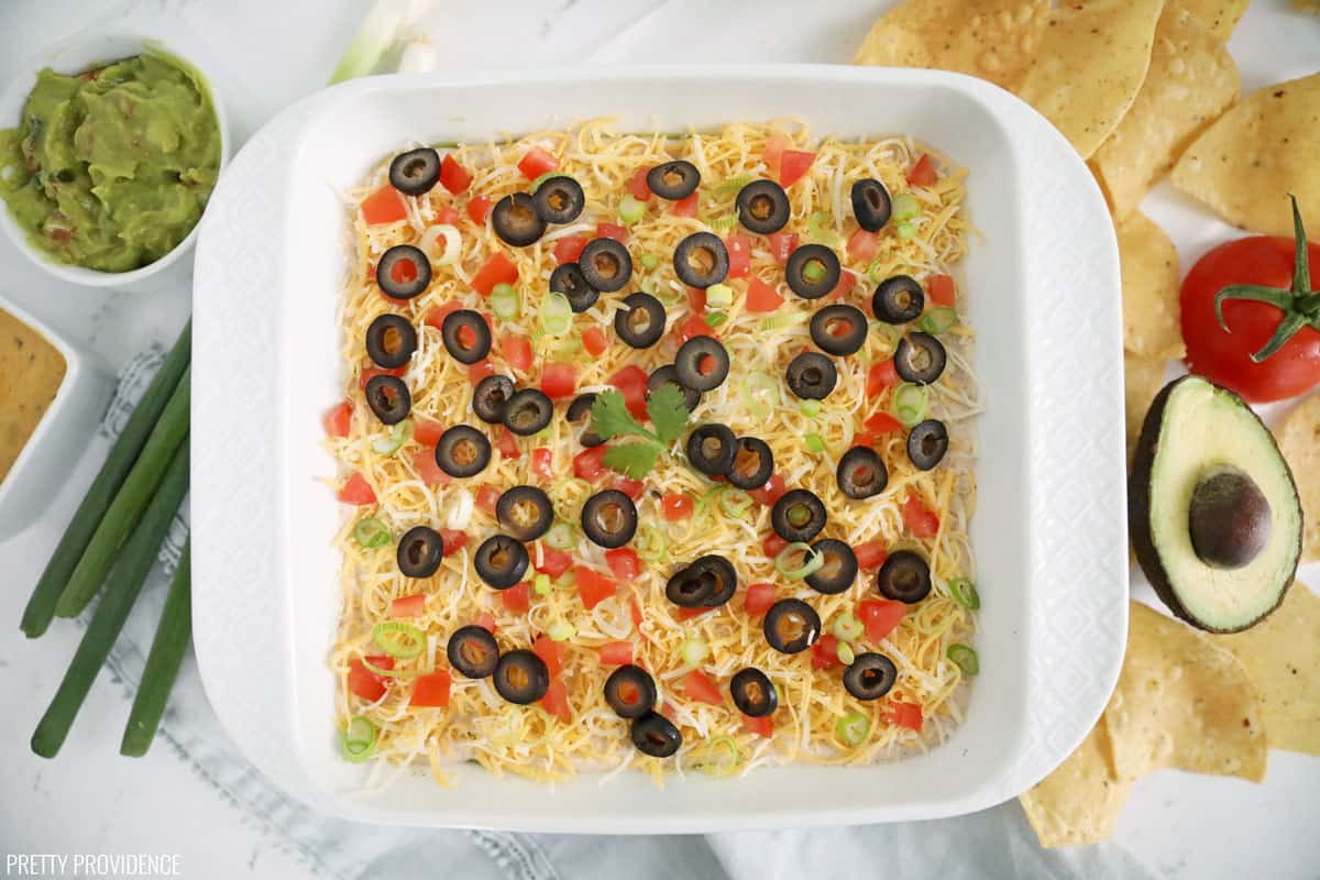 Seven layer bean dip overhead shot, with green onions, tomato, avocado and chips surrounding it