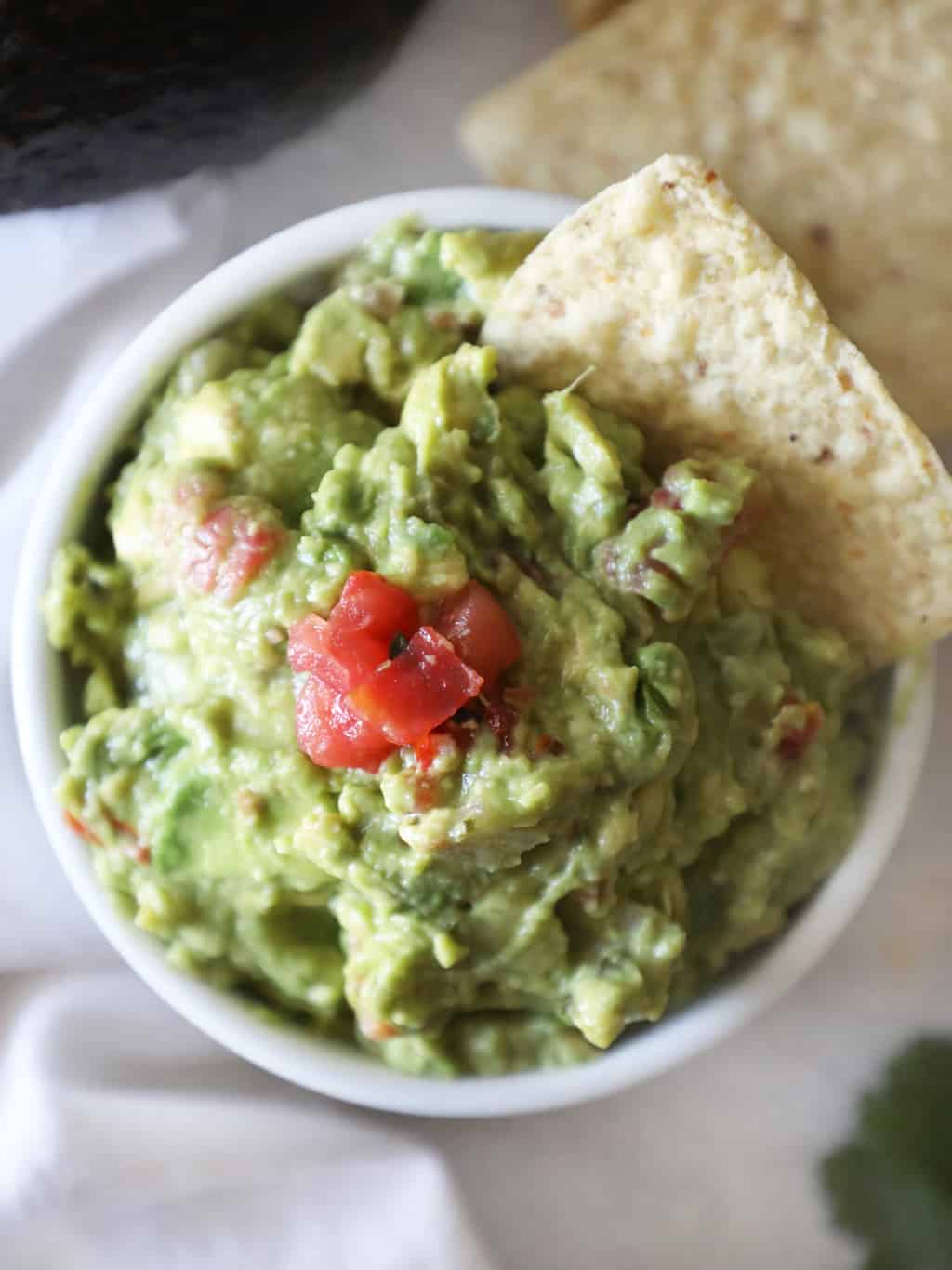 homemade guacamole in a white bowl with a chip sticking out of it