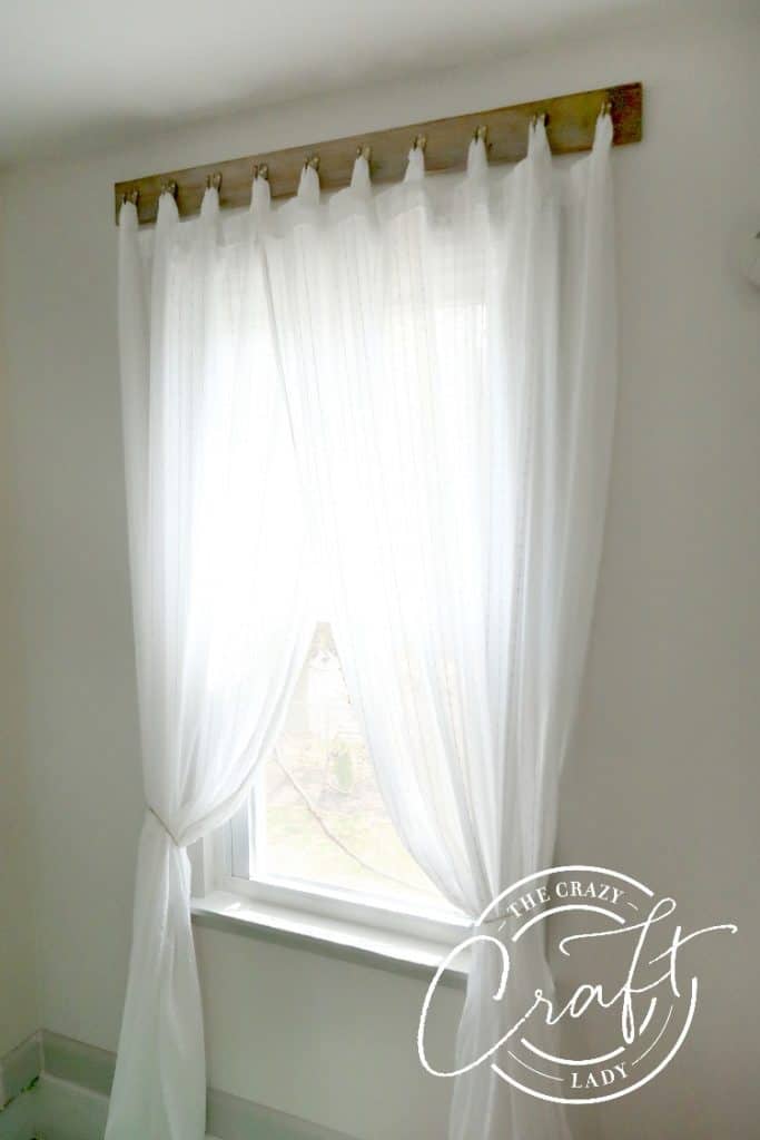 Reclaimed wood with hooks holding white curtains over a window