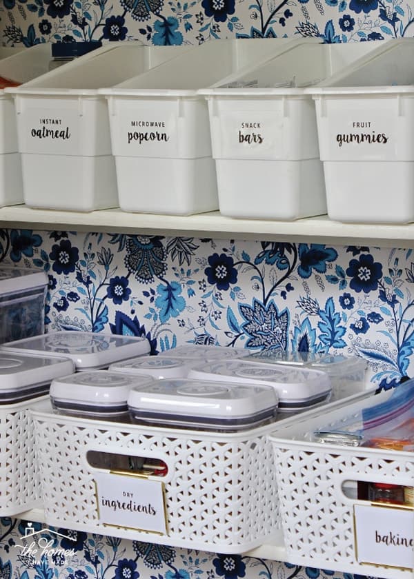 Patterned wrapping paper as wallpaper in pantry with white organizing bins