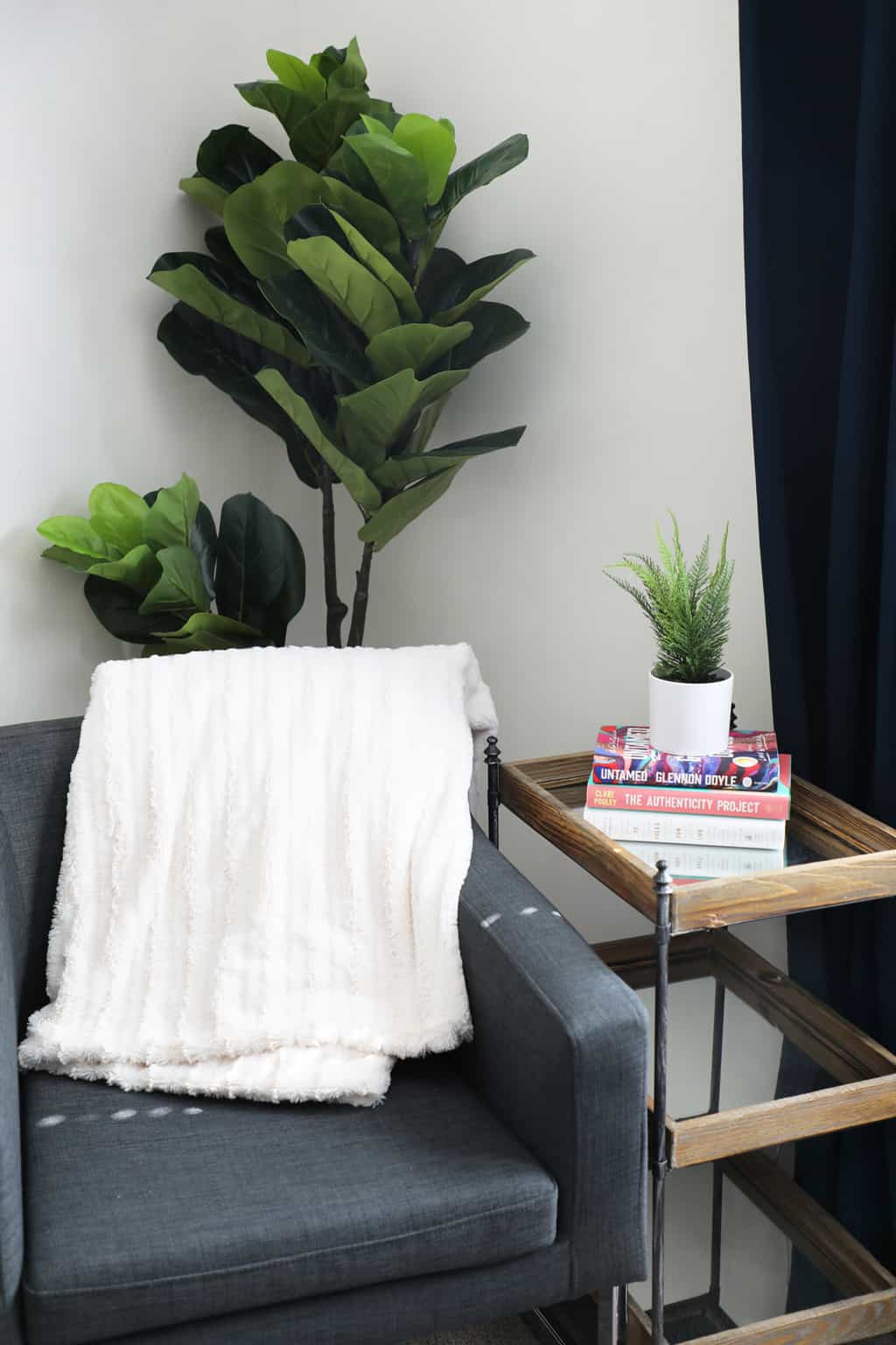 a blue chair with a white blanket in a corner with a tree behind it