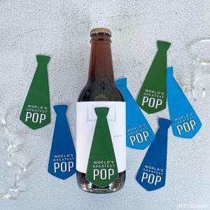 World's Best Pop tie shaped gift tags, one tag taped on a bottle of root beer