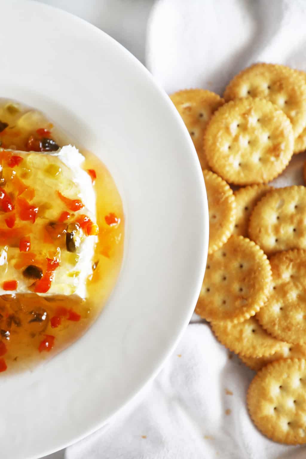 cream cheese with pepper jelly poured over it on a white plate with a bunch of crackers next to it