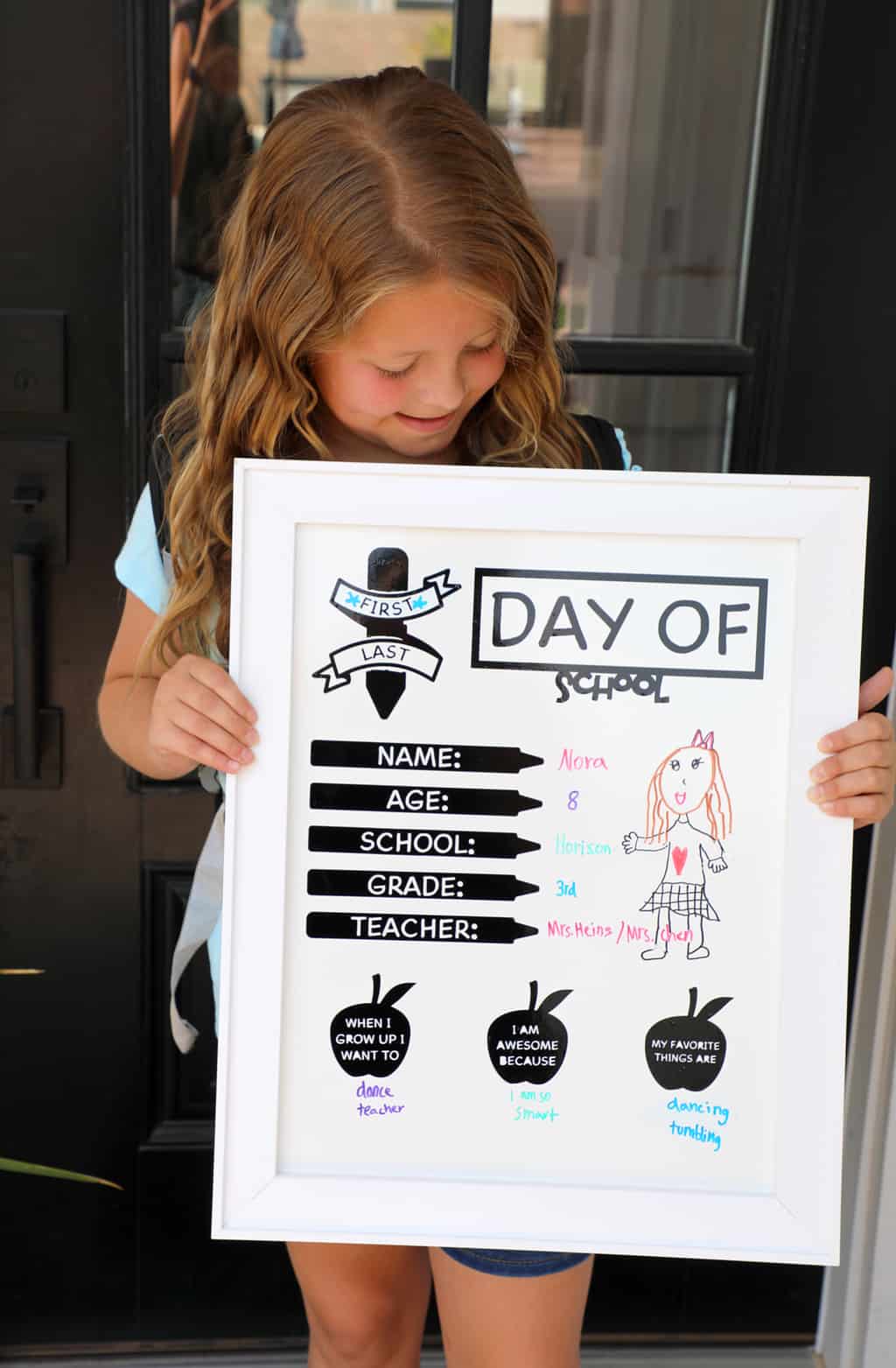 girl in front of a black door holding up a first day of school whiteboard