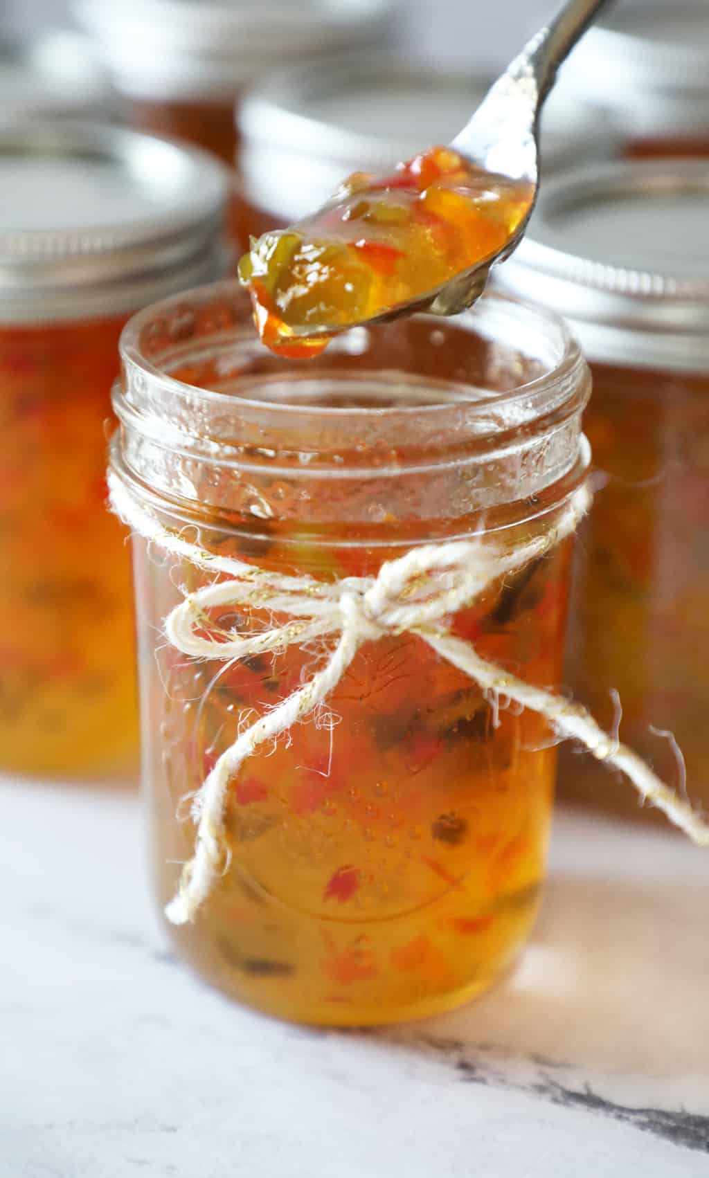 a jar of pepper jelly tied with twine with a spoon with jelly hovering above it