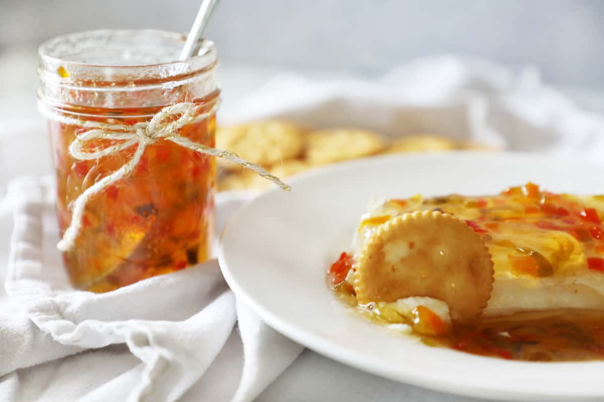 a jar of pepper jelly next to a plate of cream cheese with pepper jelly and crackers