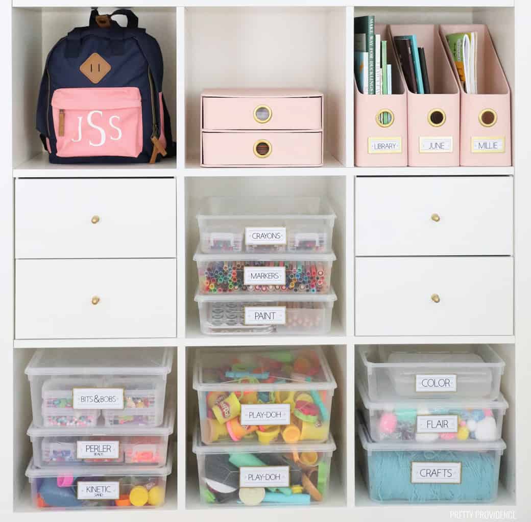 Cube shelf with clear bins full of kids art supplies labeled 