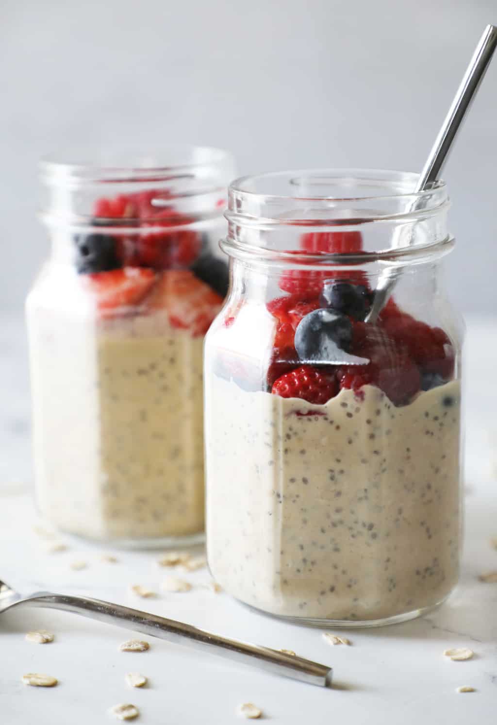 two jars of protein overnight oats with berries on top of a white counter
