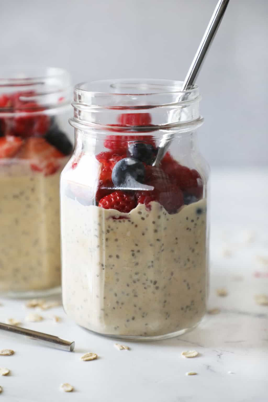 two glass jars with protein overnight oats with a spoon sticking out of one jar