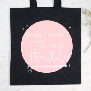 Black tote bag with pink circle and 'double double toil and trouble' in cursive white lettering on it
