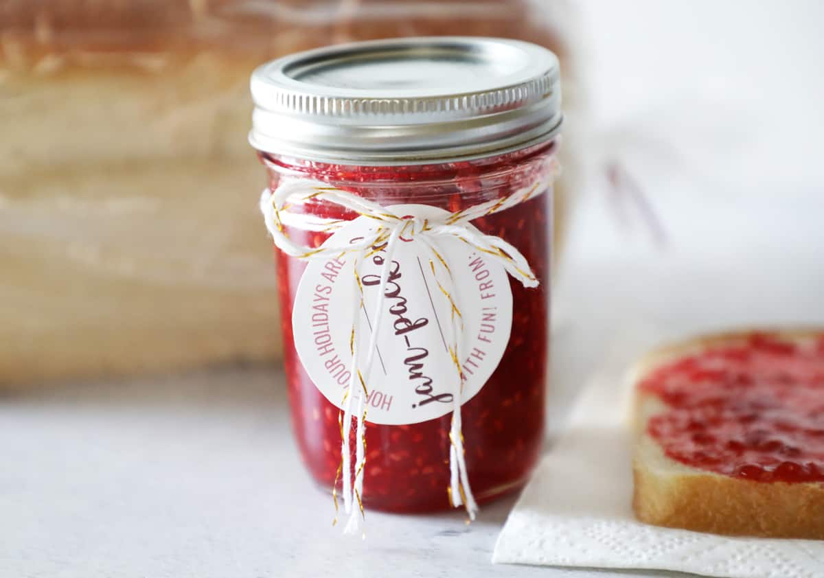 raspberry jam with jam label tied on with bakers twine in front of bread