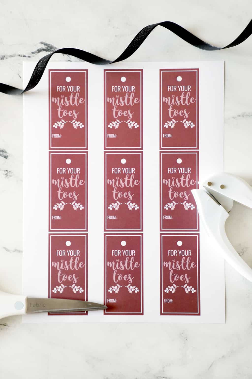 for your mistletoes printable tags next to a hole punch and black ribbon
