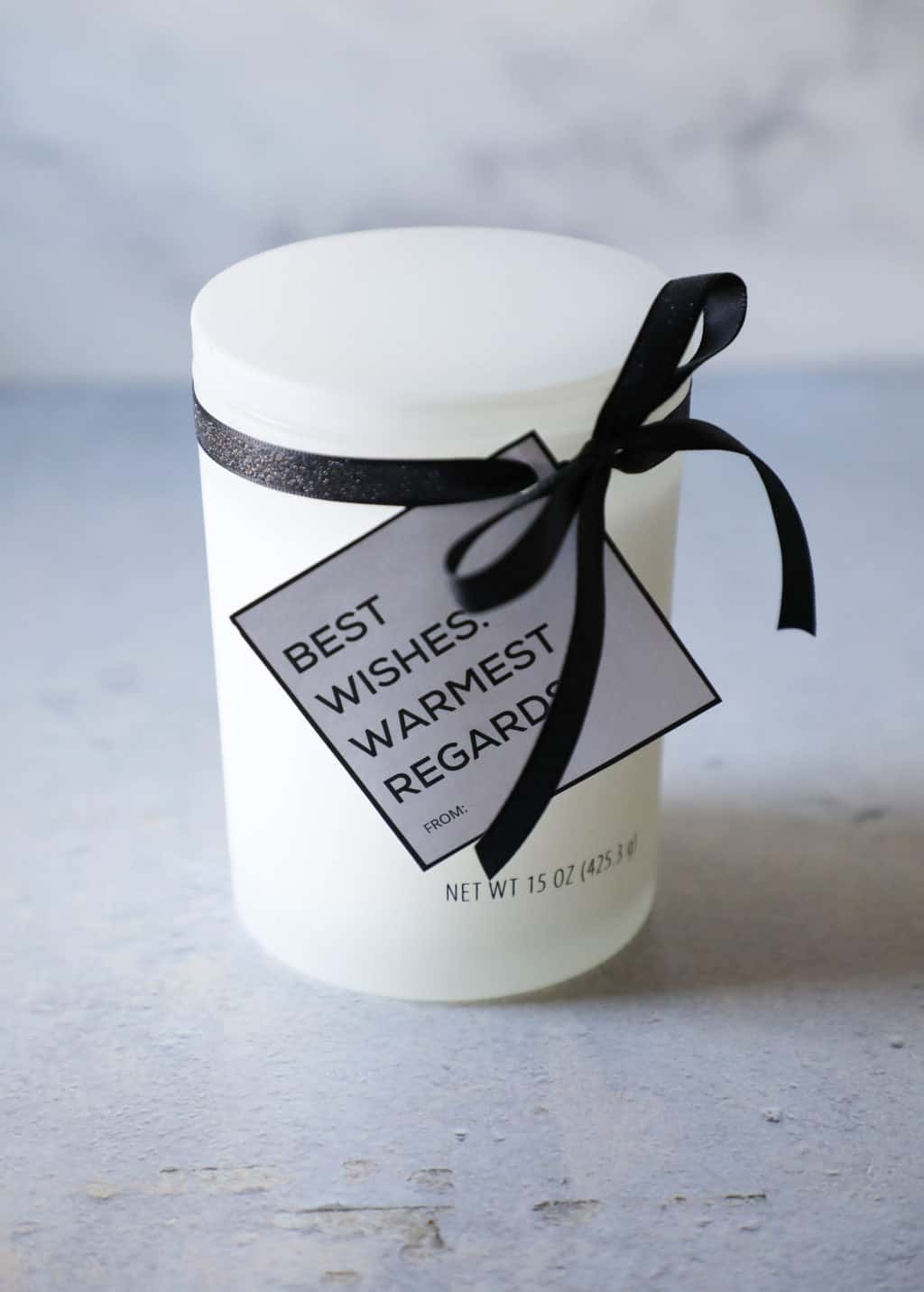 a white candle with a black ribbon and a black and white gift tag
