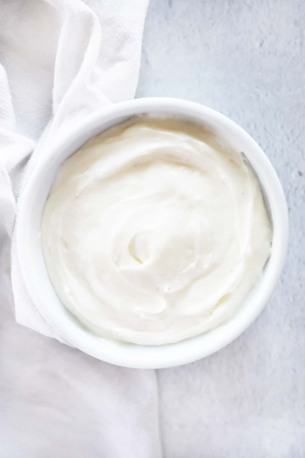 cream cheese frosting in a white bowl on a cement countertop
