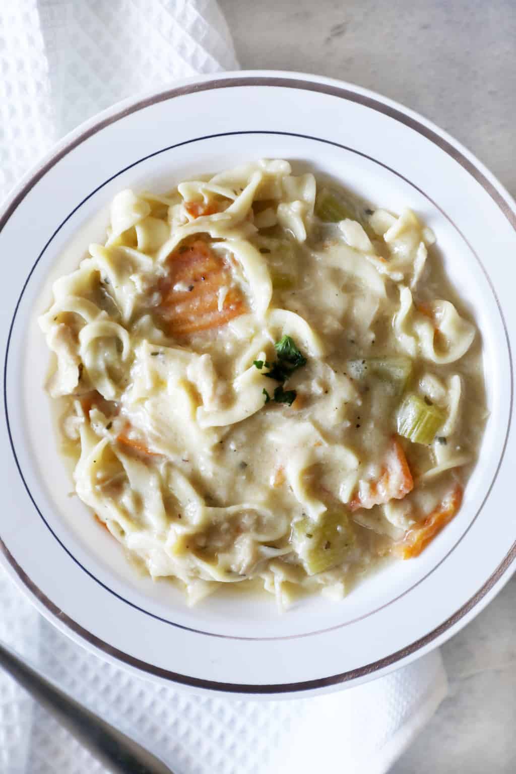 a white bowl of chicken noodle soup next to a white cloth napkin