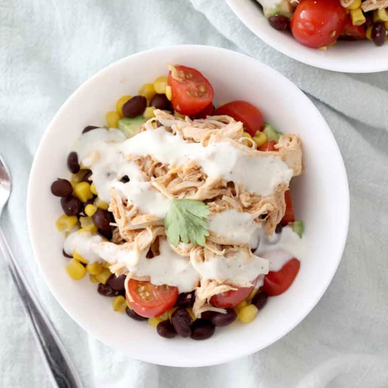 buffalo chicken bowl: corn, black beans and chicken in a white bowl topped with ranch dressing, tomatoes and cilantro