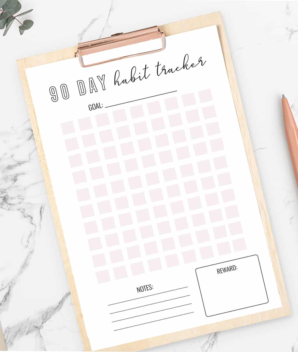 a pink and black habit tracker on a wooden clipboard laying on a marble counter