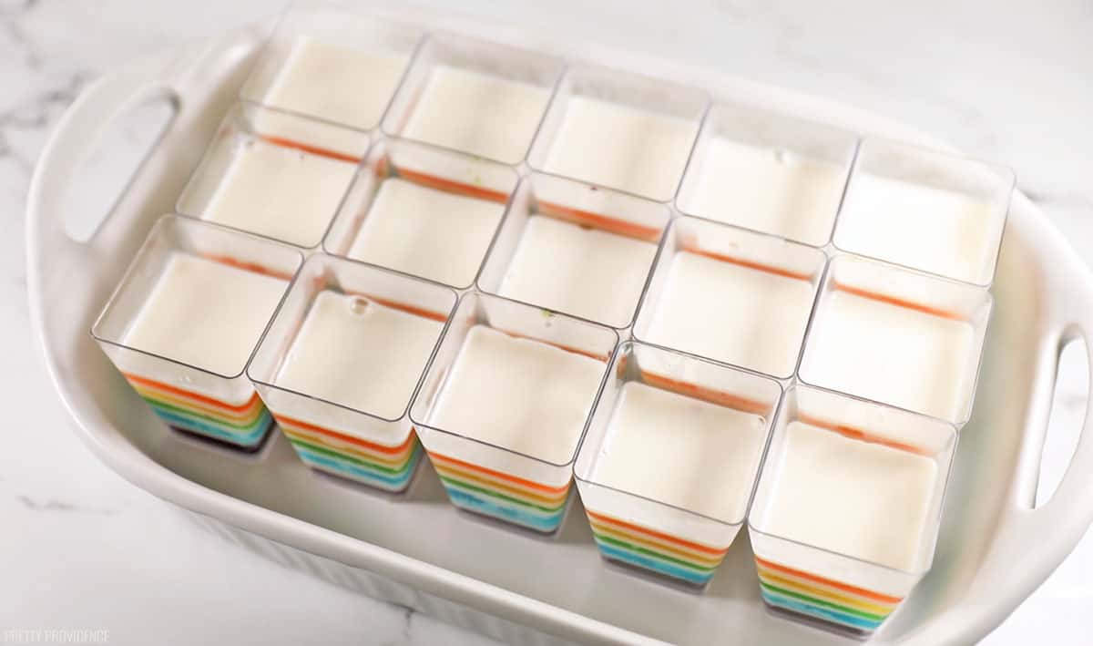 rainbow jello cups with white layers in between the colors in individual clear cups