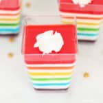 Rainbow jello layered in a clear square cup with a dollop of whipped cream on tp