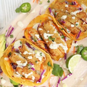 Breaded cod fish tacos on corn tortillas with toppings surrounding them