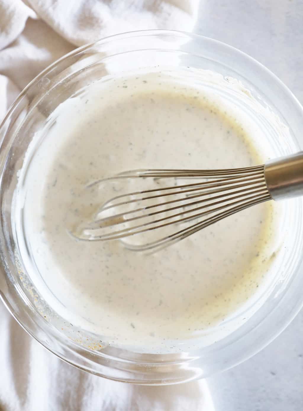 a glass bowl of homemade ranch being stirred by a whisk