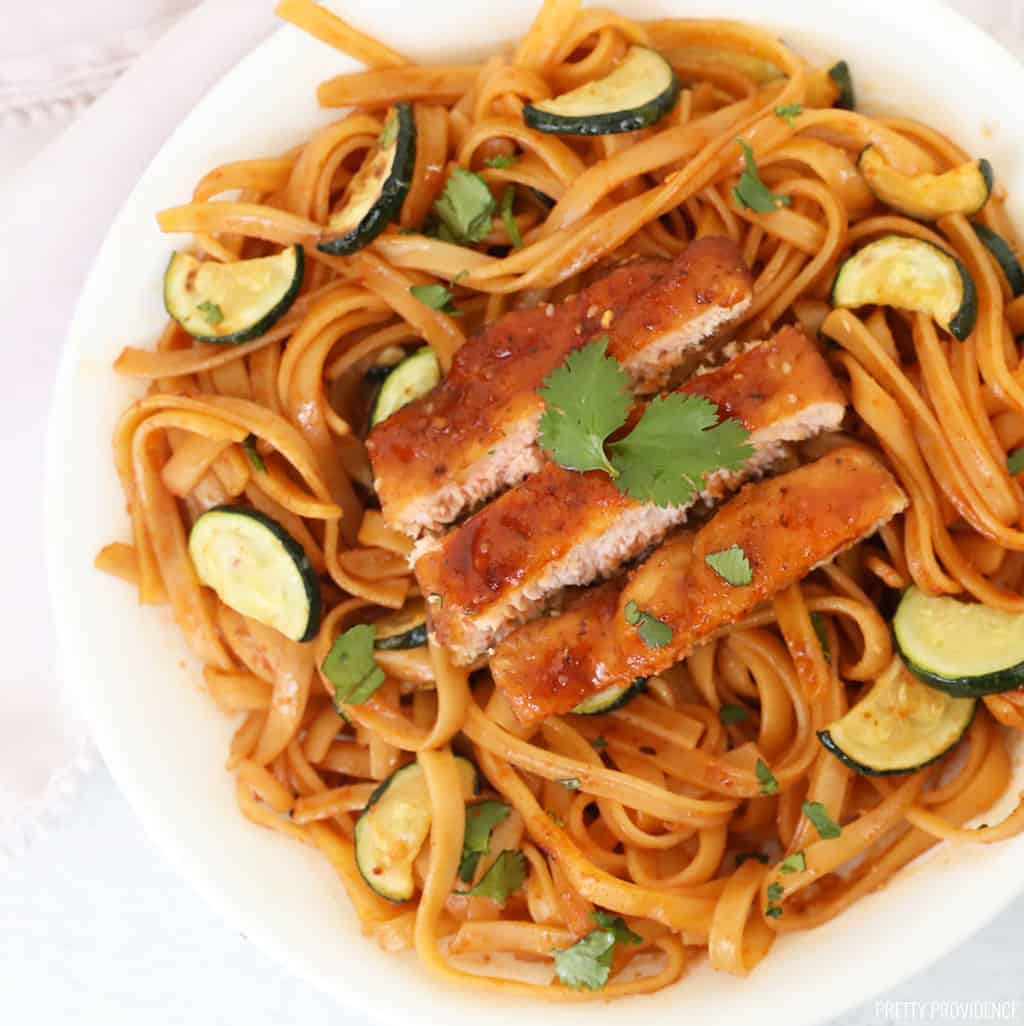 spicy noodles in a white bowl with salmon and zucchini