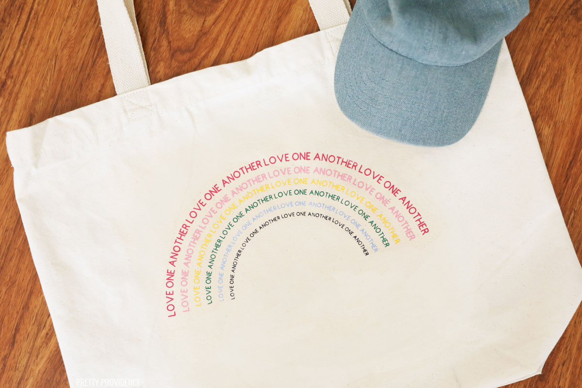 Canvas tote bag with a rainbow made out of the words 'Love One Another'