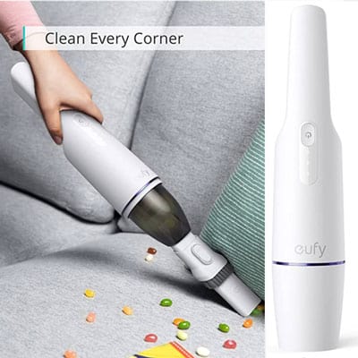 White handheld vacuum picking up crumbs from a gray couch