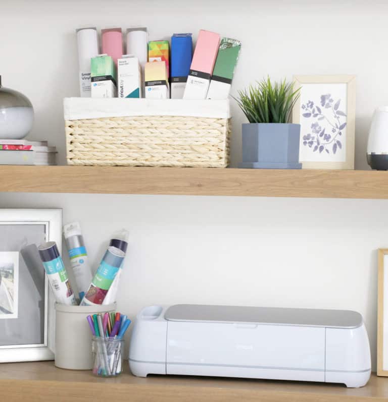 light blue Cricut maker 3 next to vinyl and art on shelves