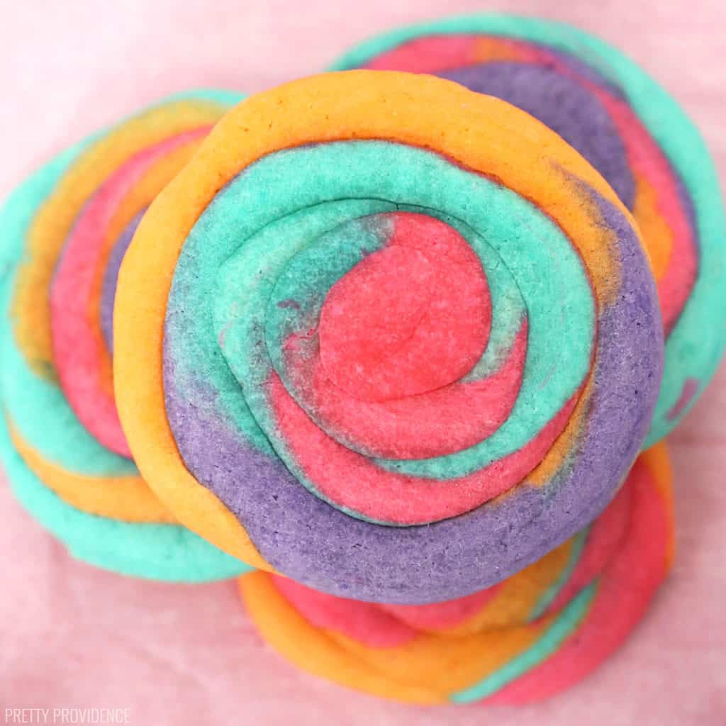 Tie Dye Sugar Cookies (bright pink, orange, purple and teal) stacked on top of each other on a pink parchment paper sheet