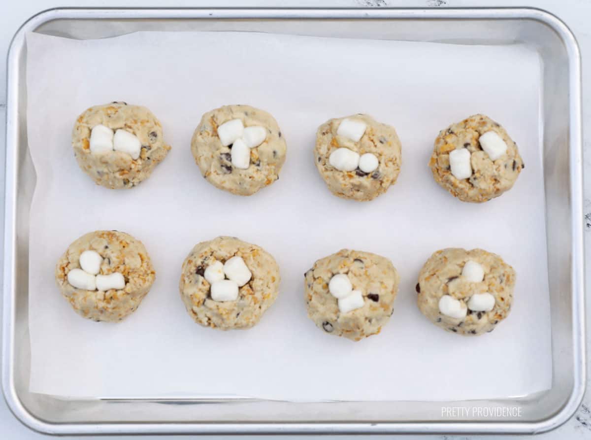 cookie dough with marshmallows and chocolate chips on a cookie sheet
