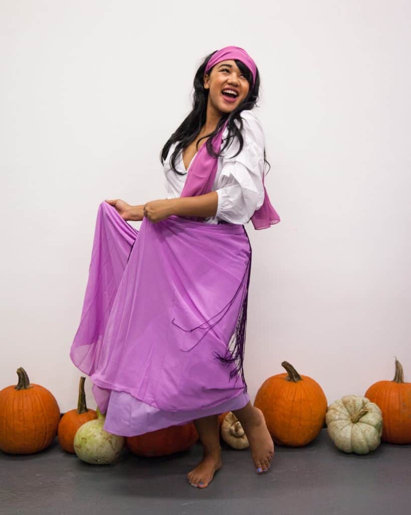 Esmerelda costume for women wearing a purple headband, purple dress and white puffy sleeved blouse.