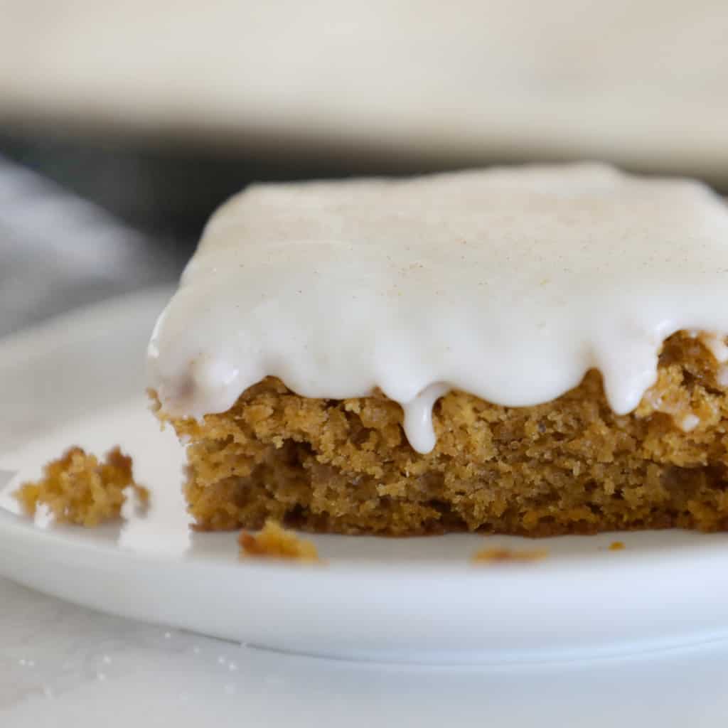 close up of a slice of pumpkin sheet cake with cream cheese icing dripping over the side