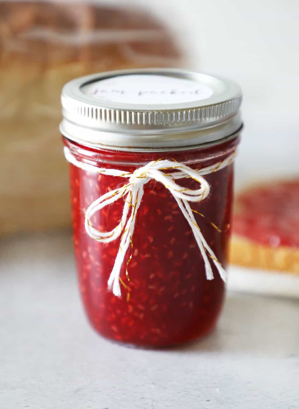 a small jar of jam wrapped with twine in front of a loaf of bread