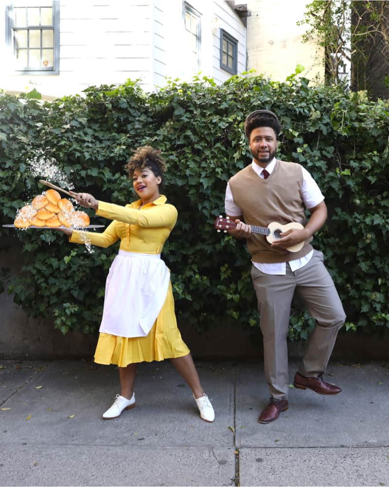 Woman dressed as Tiana in a yellow dress and white apron, a man dressed as Prince Naveen with a Ukulele. The Princess and the Frog couples costumes.