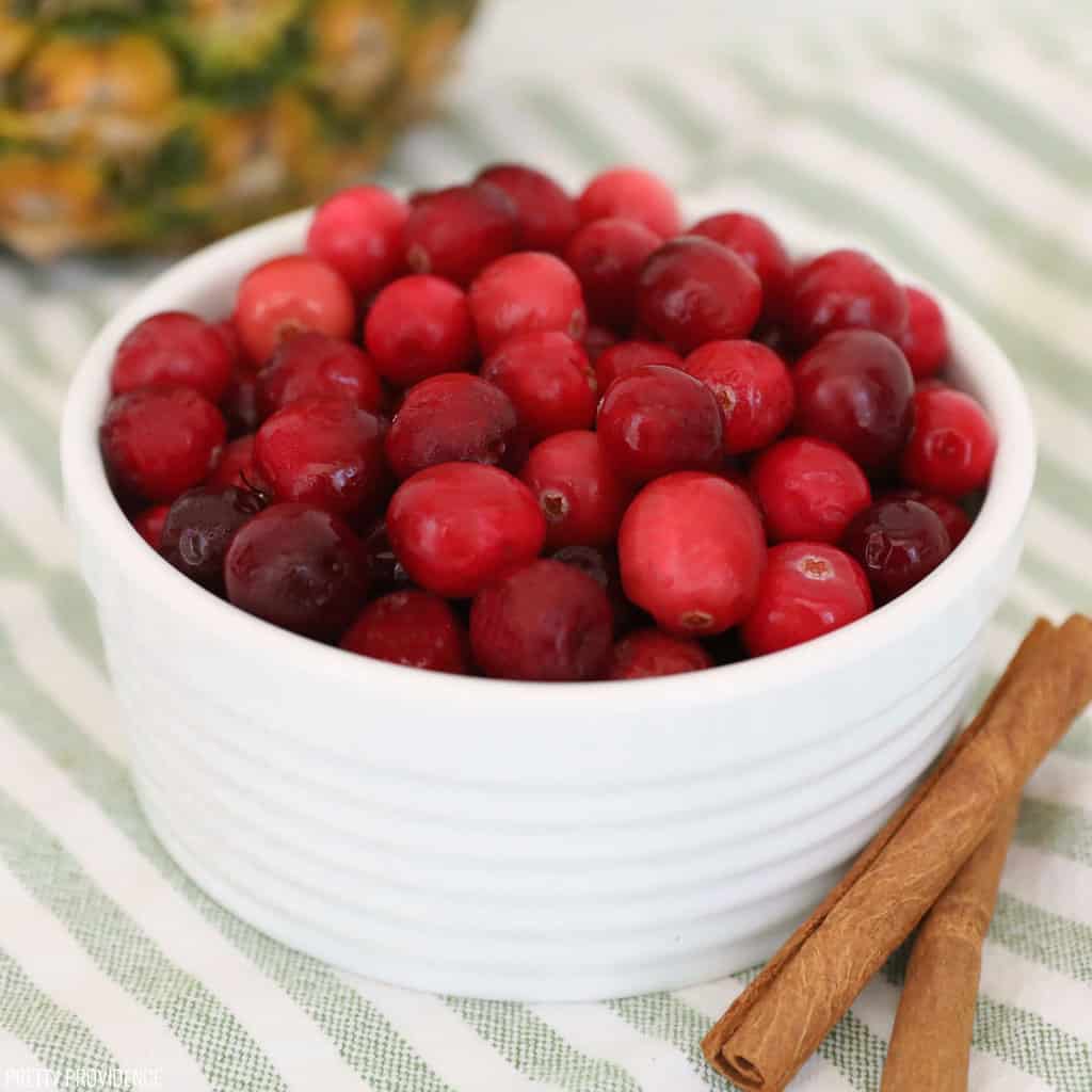 fresh cranberries in a white dish with cinnamon sticks on a striped green and white dish towel