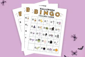Free printable Halloween Bingo cards with traditional Halloween images like black cat, pumpkin, bat, spider, etc. Papers rest on a purple background.