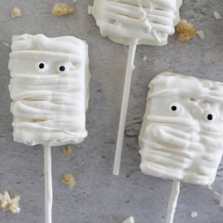 Rice Krispie treat mummies on a concrete countertop surrounded by crumbs