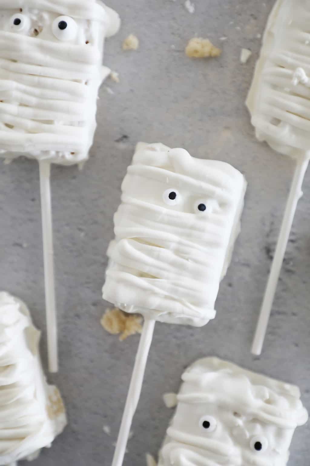 White chocolate covered mummy treats on baking sticks with candy eyes.