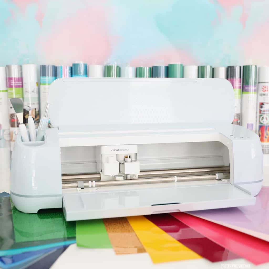 Light blue Cricut Maker 3 with an assortment of colors of vinyl and iron-on vinyl fanned out under it and behind it. 