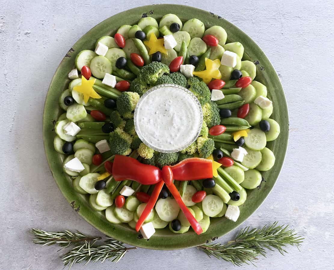 A veggie tray shaped like a wreath with rosemary at the bottom to garnish.