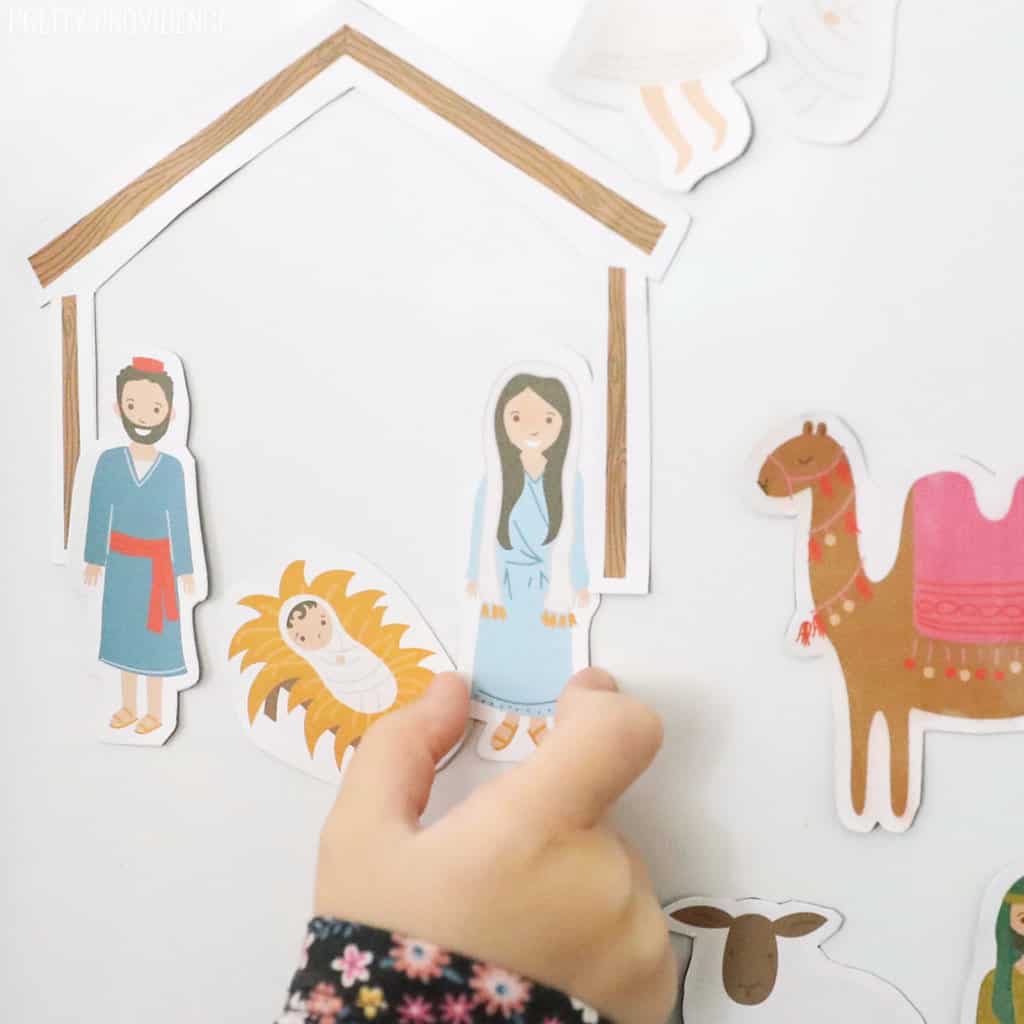 magnetic nativity set on a white fridge with a child's hand putting a magnet