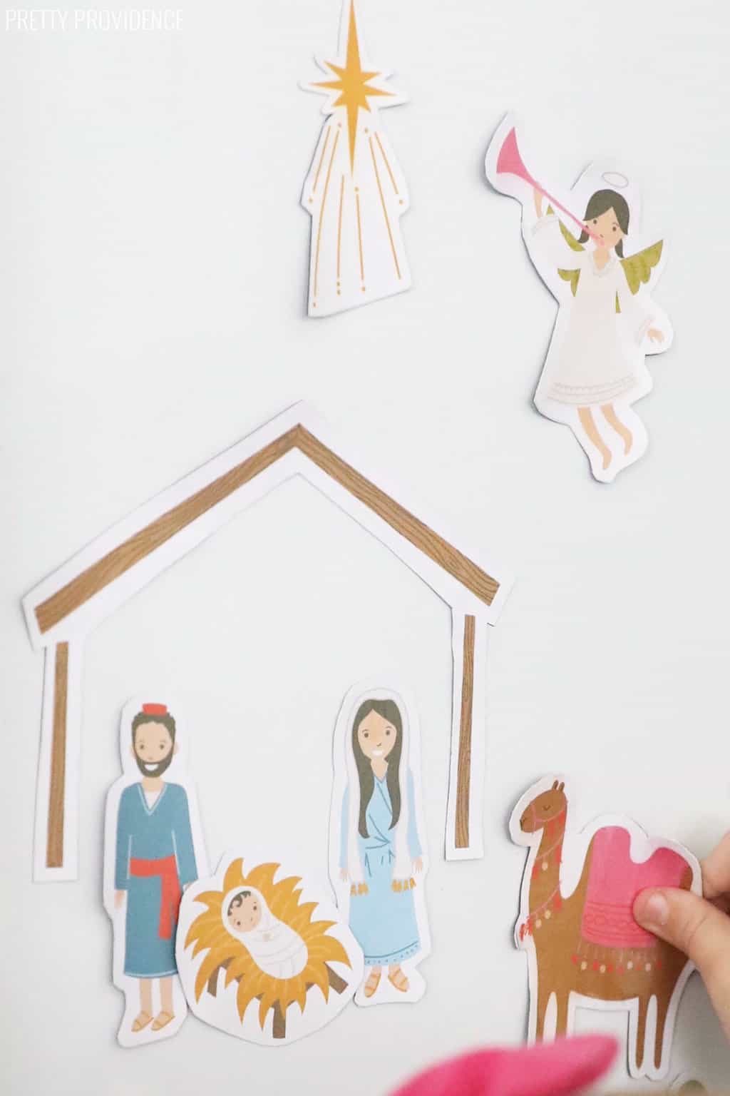 magnetic nativity set on a white fridge with a little hand putting a camel magnet on.