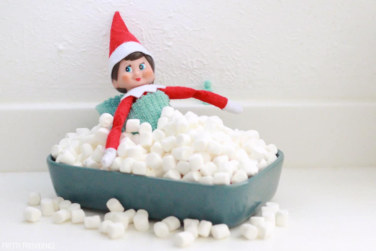 Elf on the shelf having a bubble bath in a tub marshmallows.
