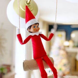 Elf on the shelf on a swing made from twine and a toilet paper roll.