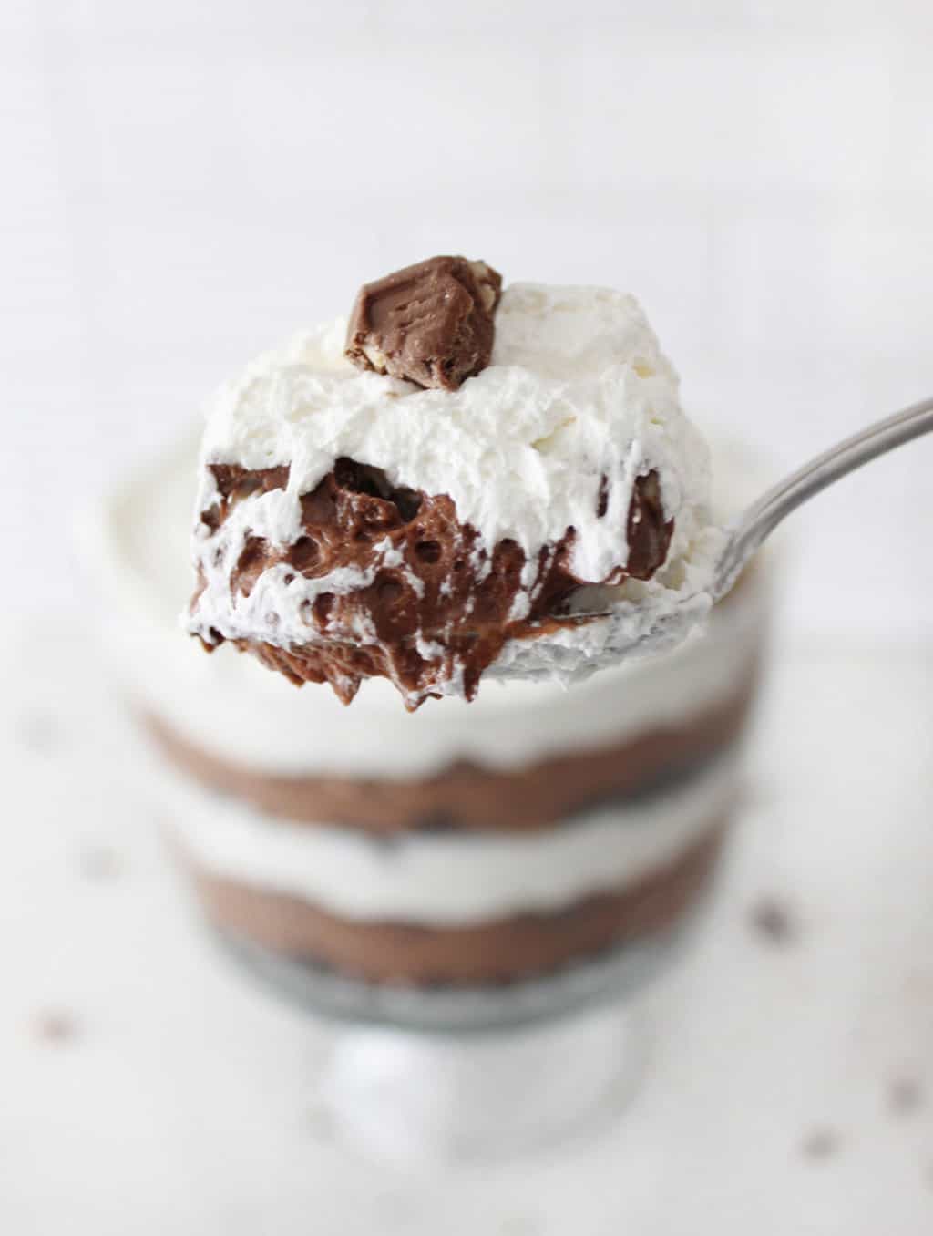 A spoon with a bite of chocolate layered trifle on it.