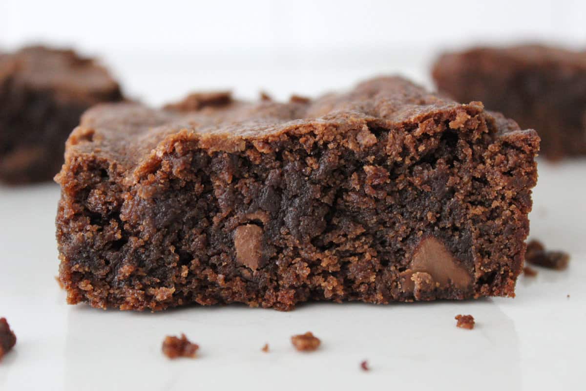 A side view image on a homemade brownie with some crumbs surrounding it. 