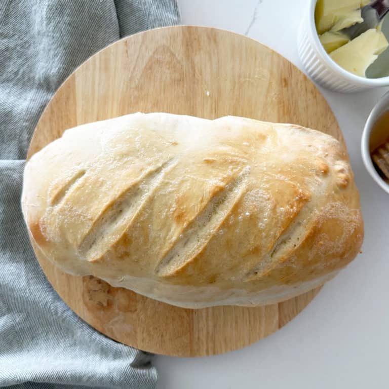 A bird's eye view of a loaf of rustic French bread on a round wooden cutting board.