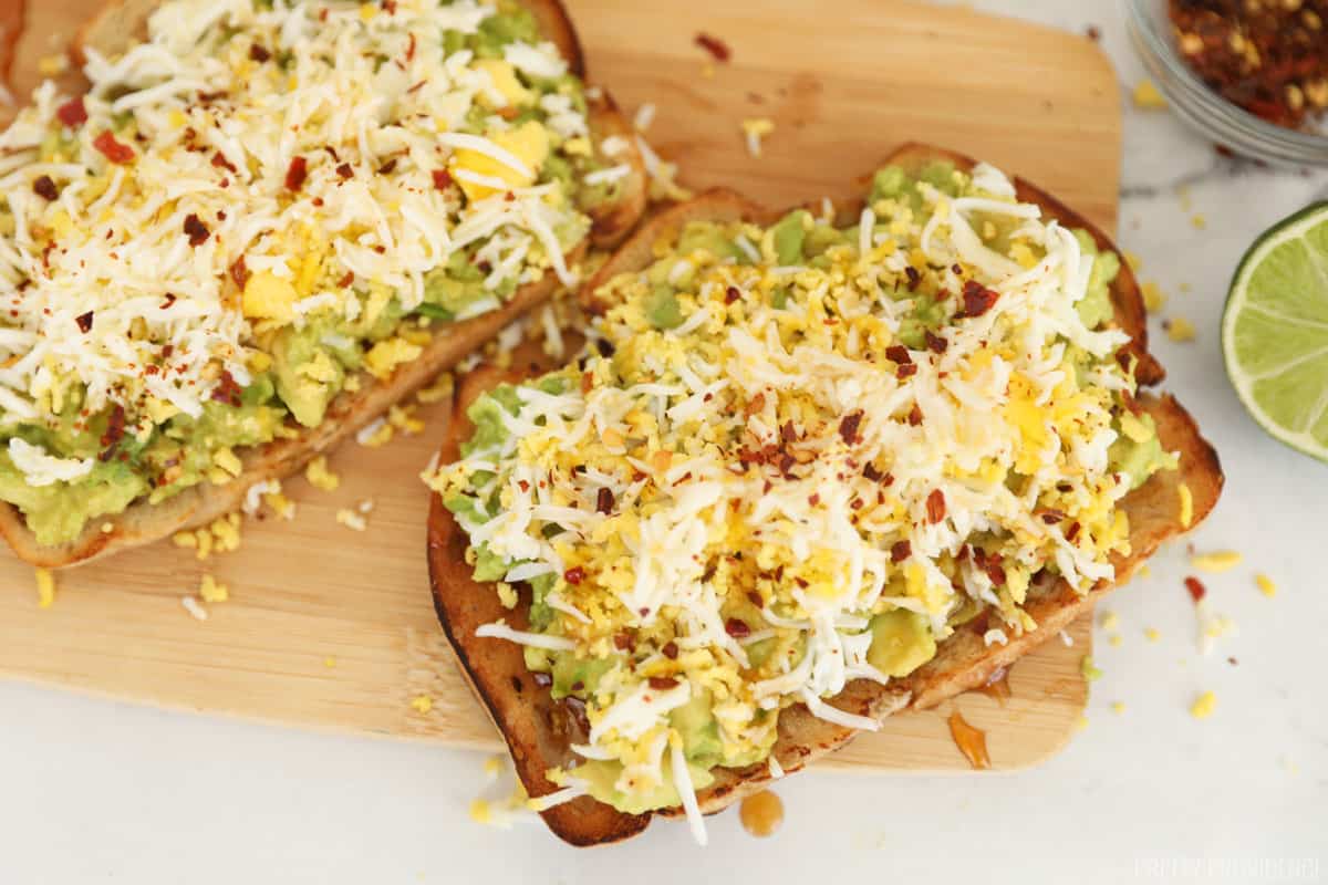 Avocado toast with egg grated and red pepper flakes on top resting on a cutting board.